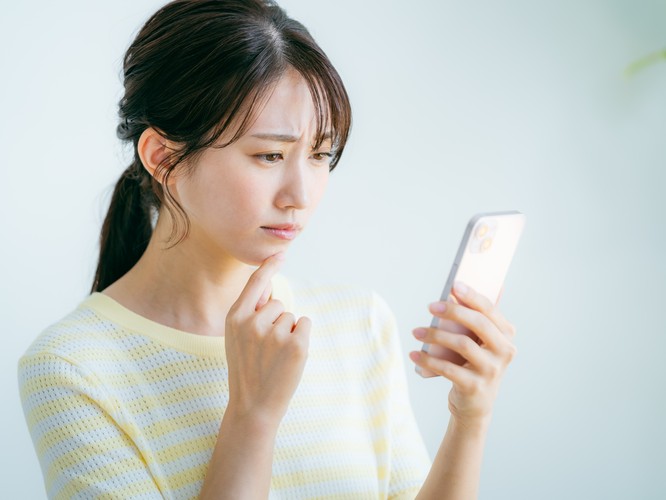スマホの画面を見て悩む女性